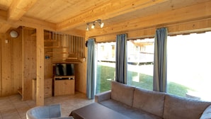 A wooden interior with a sofa, chairs, a TV, and a small kitchen area.