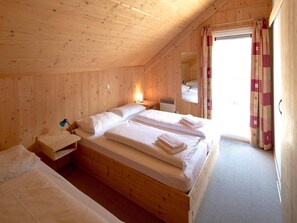 Une pièce de cabane en bois comprenant deux lits, une petite table et une fenêtre avec des rideaux.