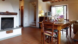 A spacious living room with a fireplace, wooden dining table, and comfortable seating. A staircase leads to an upper level. - Holiday Home in Montecarelli with Pool (Montecarelli)
