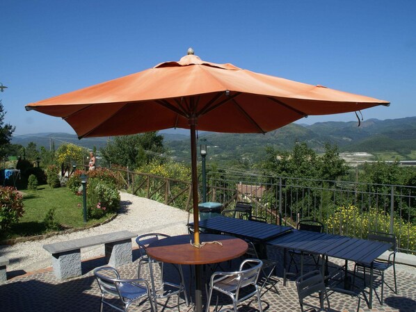 A terrace with outdoor seating, a large umbrella, and a scenic mountain view.