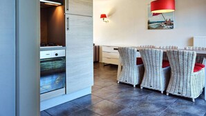 Eine moderne Küche mit Backofen und einem Essbereich mit Korbstühlen und einer roten Lampe.
