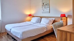Ein Doppelbett mit weißen Bettwäsche, zwei Nachttischlampen, ein Holzkopfstück, eine gewebte Tagesdecke und ein Bild an der Wand.