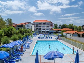 A swimming pool with lounge chairs and umbrellas, surrounded by buildings with red roofs.