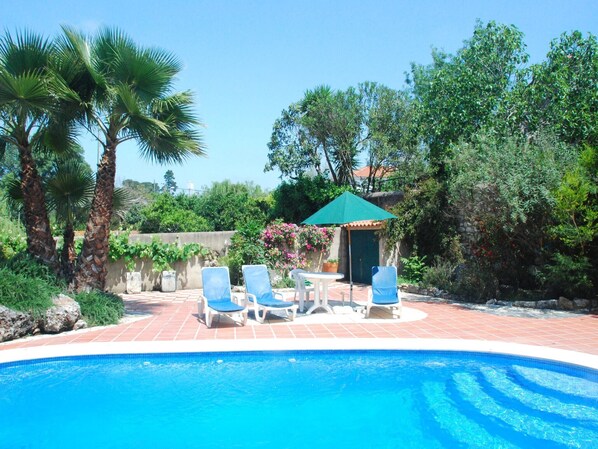 A swimming pool with blue water, surrounded by palm trees and a garden. - Vintage Farmhouse in Soudos Lisbon with pool (Soudos)