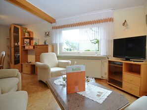 Una sala de estar con sofá, sillón, televisor y una mesa con camino de mesa.
