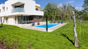 A modern two-story house with a swimming pool, outdoor seating, and a well-maintained lawn.