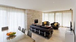 A modern living room with a stone accent wall, a black sofa, a dining table with fruit, and a TV.