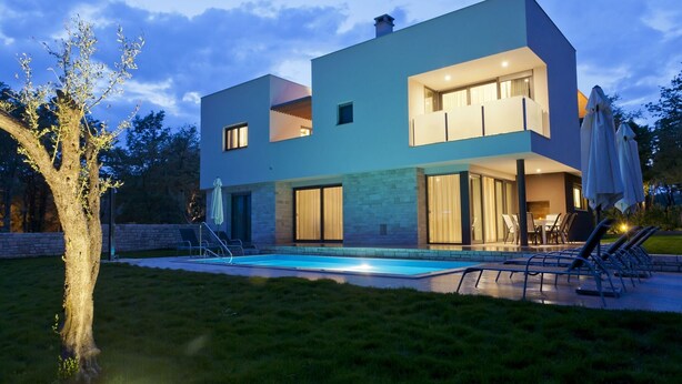 A modern two-story house with a swimming pool, outdoor seating, and a well-maintained lawn.