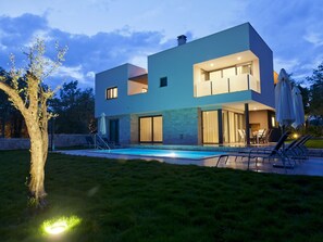 Una casa moderna de dos pisos con piscina, mobiliario de exterior y un césped bien cuidado.