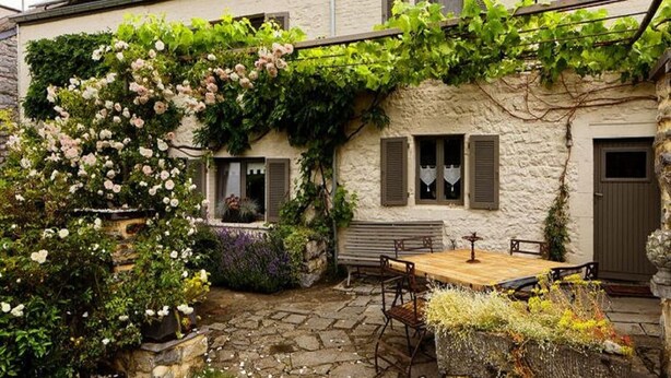 A stone building with a garden patio, a wooden table, and a bench. - Charming cottage in a farm with views (Gimnee)