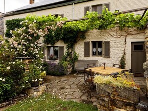 A stone building with a garden patio, a wooden table, and a bench. - Charming cottage in a farm with views (Gimnee)
