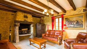 Una habitación rústica con vigas de madera a la vista, una chimenea de piedra, sofás de cuero y un cuadro grande en la pared.