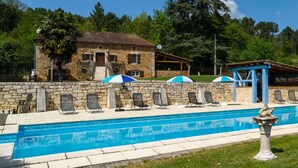 Un edificio de piedra con piscina, mobiliario exterior y sombrillas.