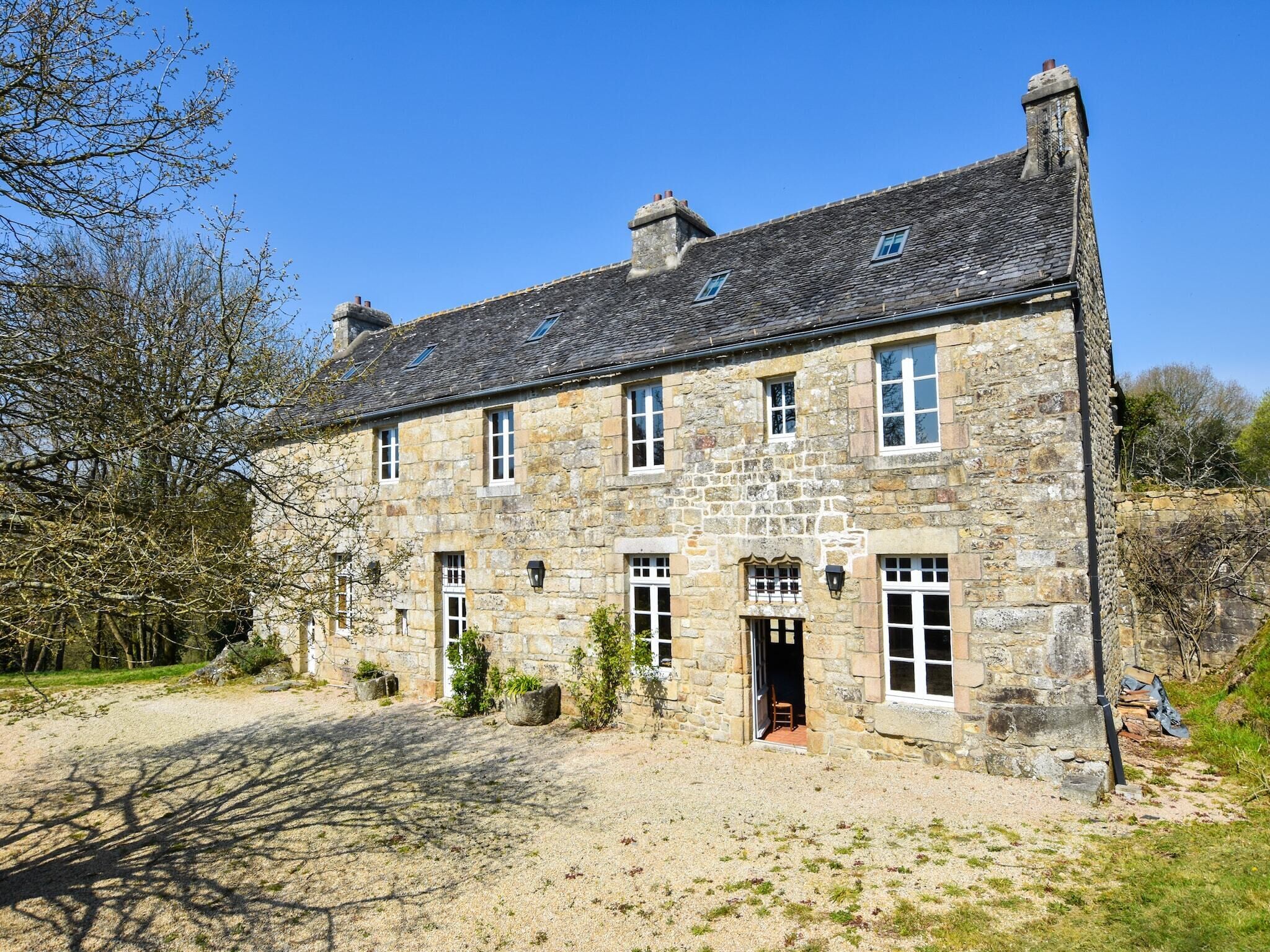 A stone building with multiple windows and a door, surrounded by a gravel driveway and sparse vegetation.
