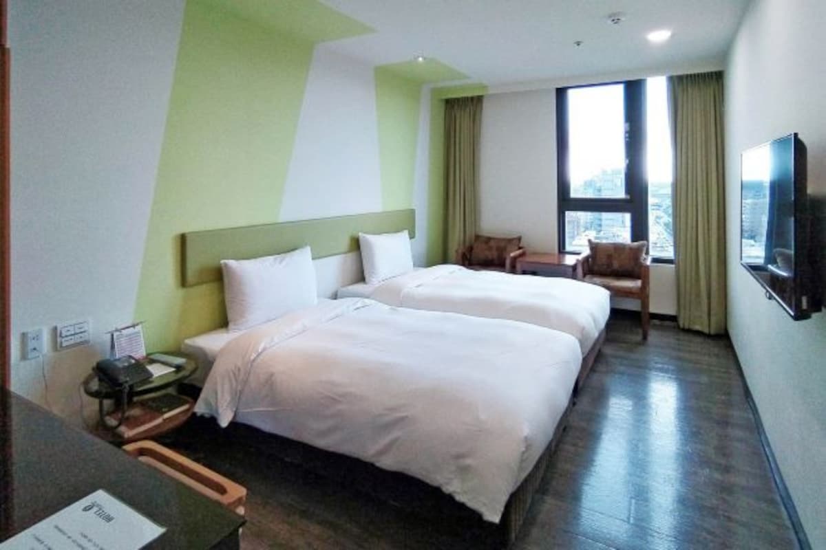 A hotel room with two beds, a desk with a telephone, and a TV on the wall.