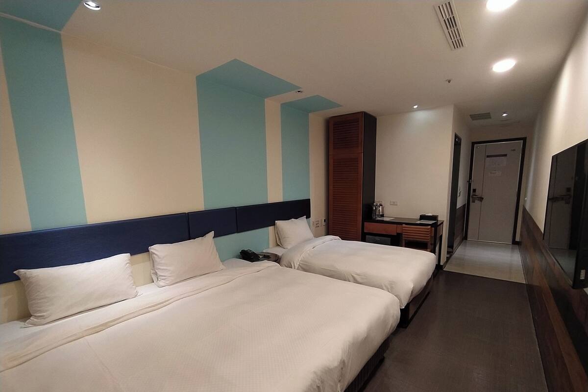 Una camera d'albergo con due letti, una scrivania e uno specchio.