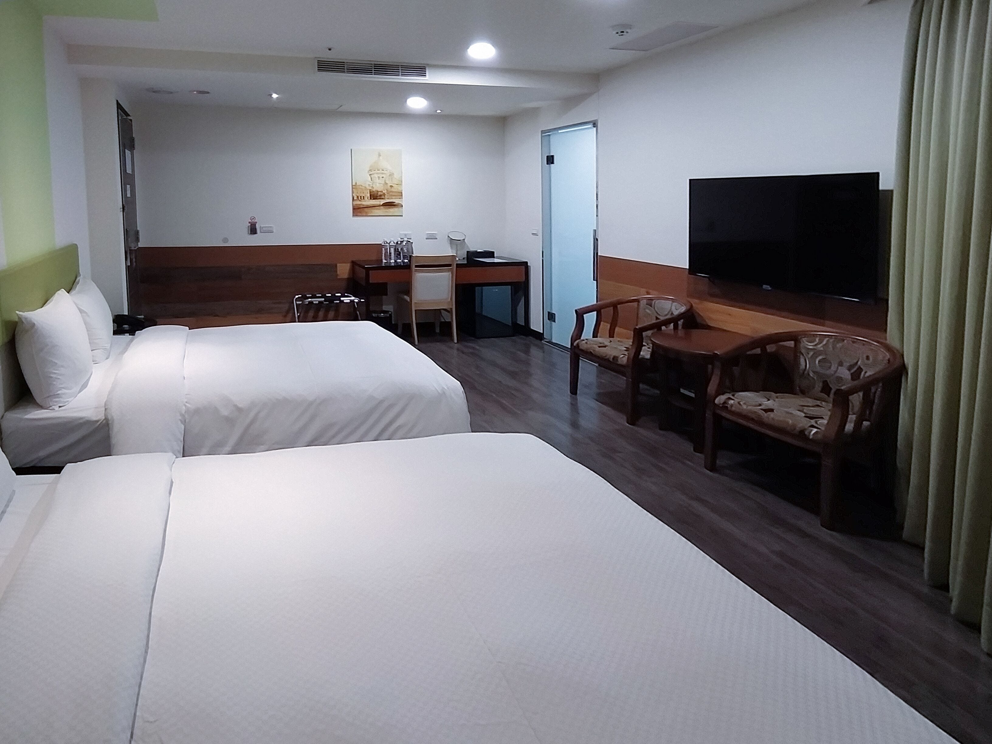 A hotel room with two beds, a desk, a chair, a television, and a door.