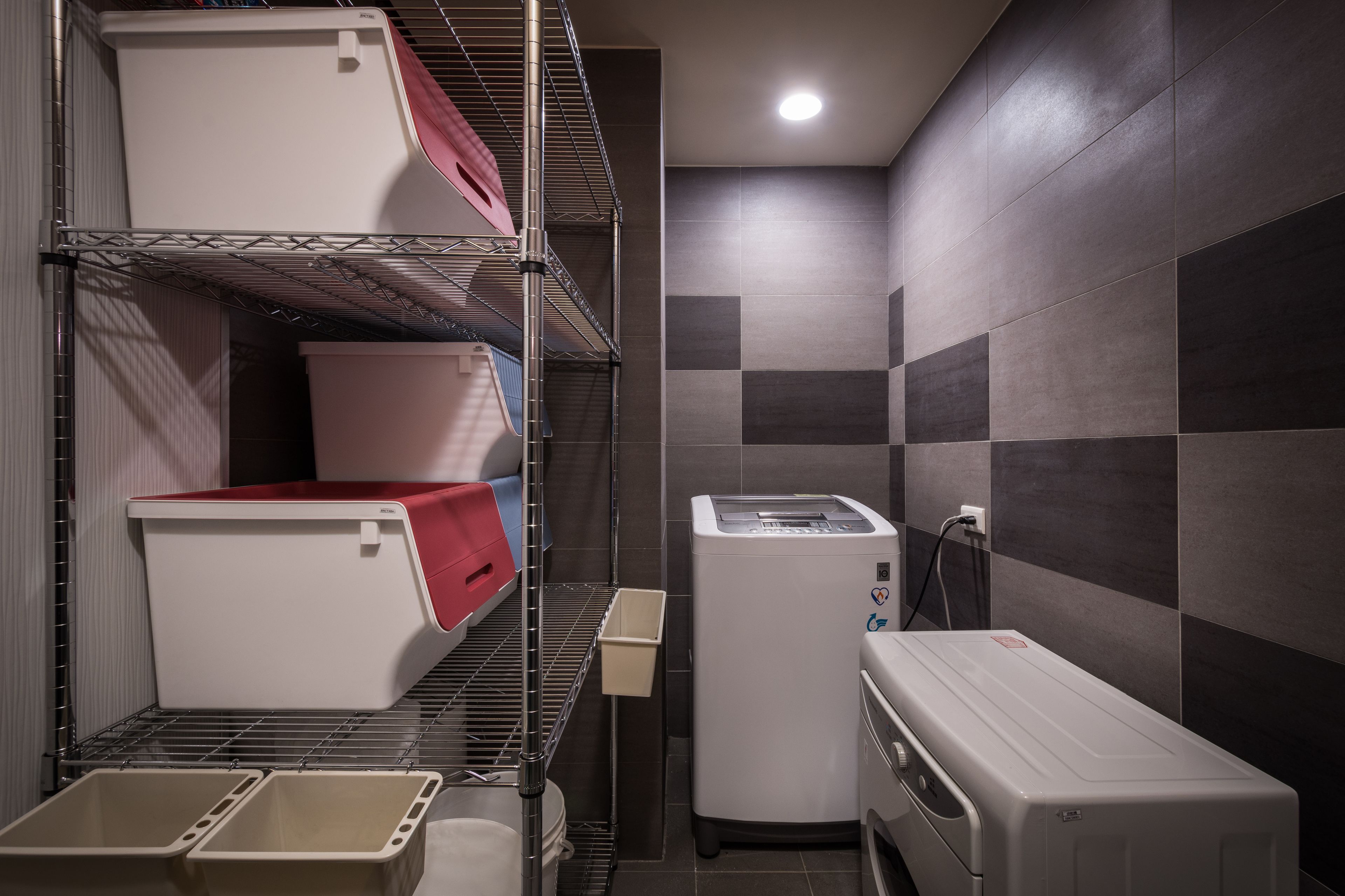 Un cuarto de servicio compacto con estantes metálicos, una lavadora blanca y un refrigerador pequeño.