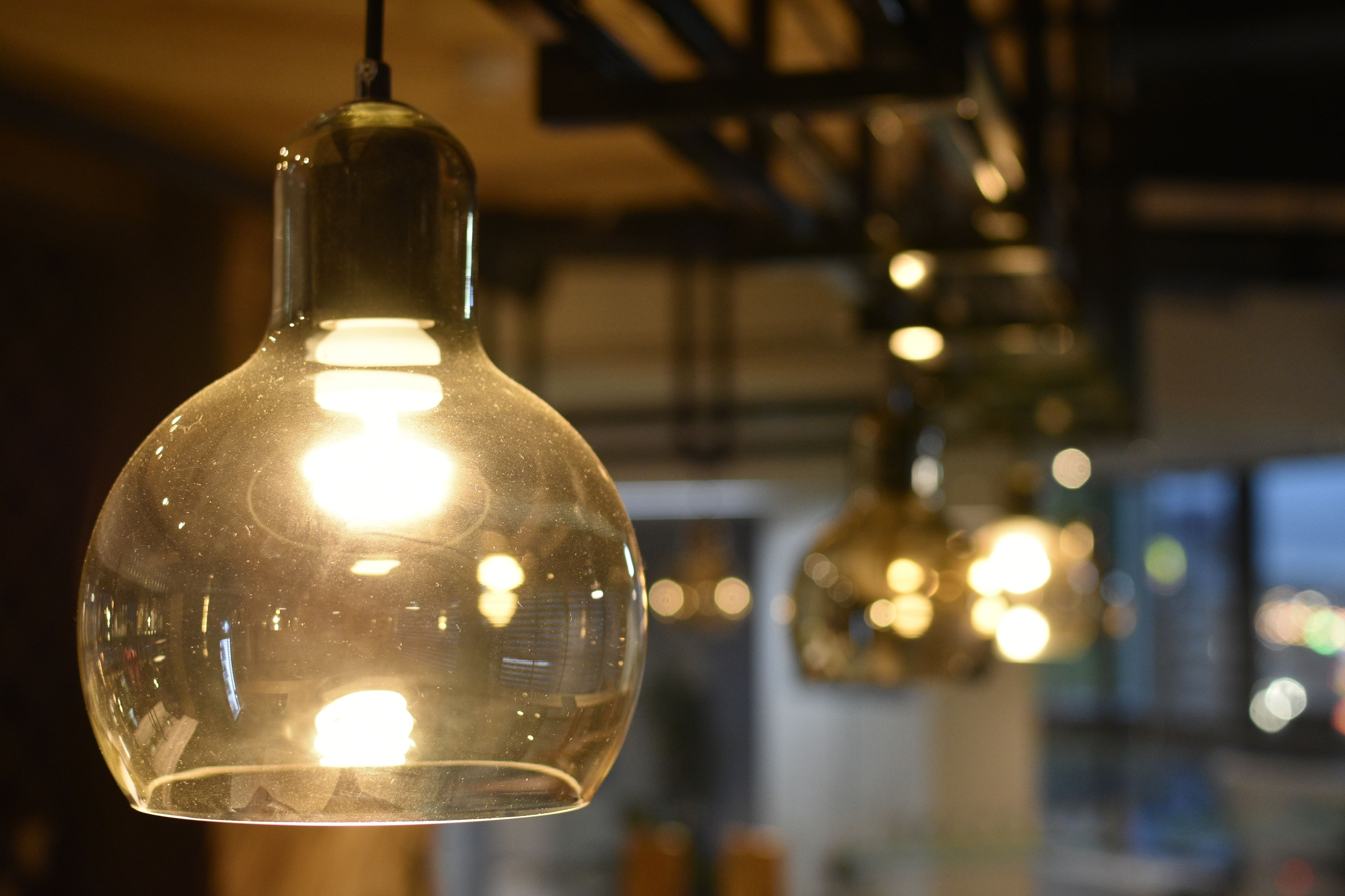 A close-up of a clear glass pendant light with a warm glow, hanging in a dimly lit interior space.