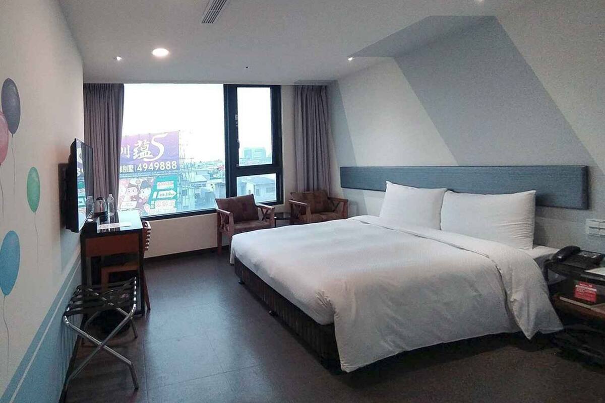 Una camera d'albergo con un letto grande, una scrivania con una sedia, una televisione e una finestra con tende.