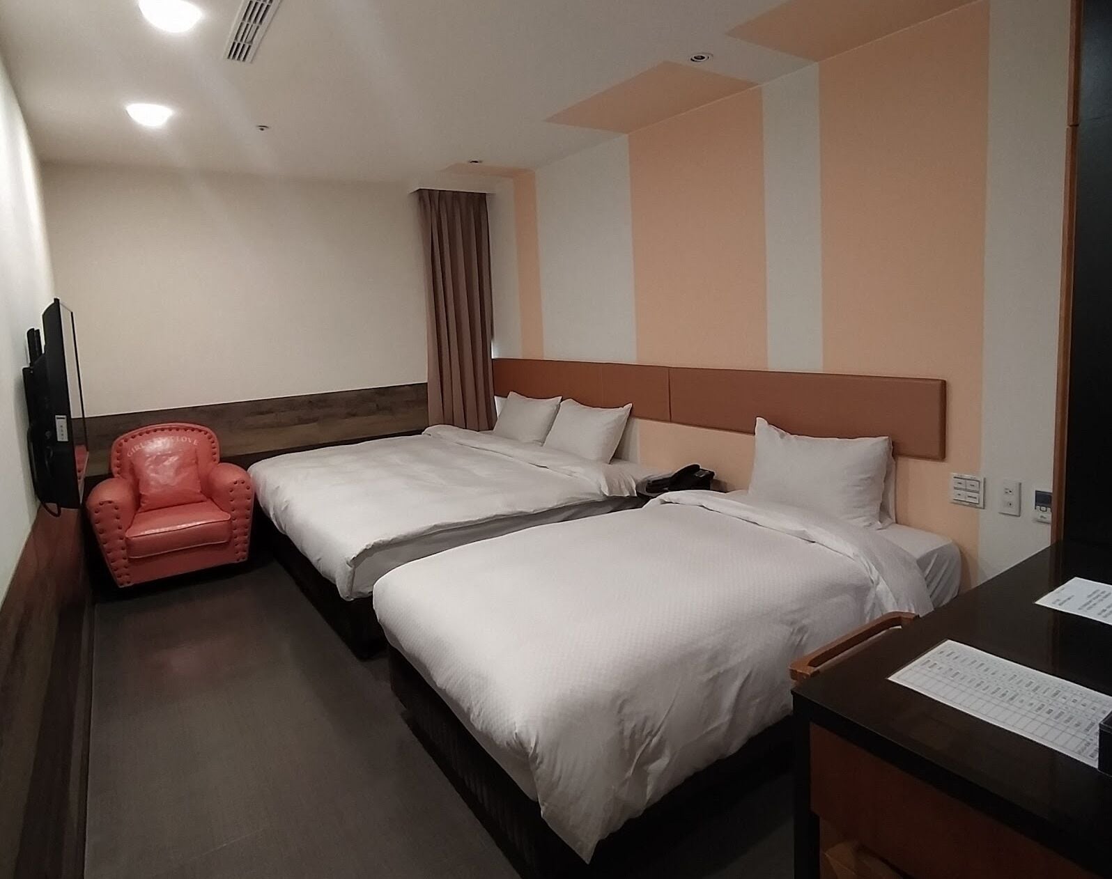 Ein Hotelzimmer mit zwei Betten, einem roten Sessel, einem Schreibtisch und einem Fernseher.