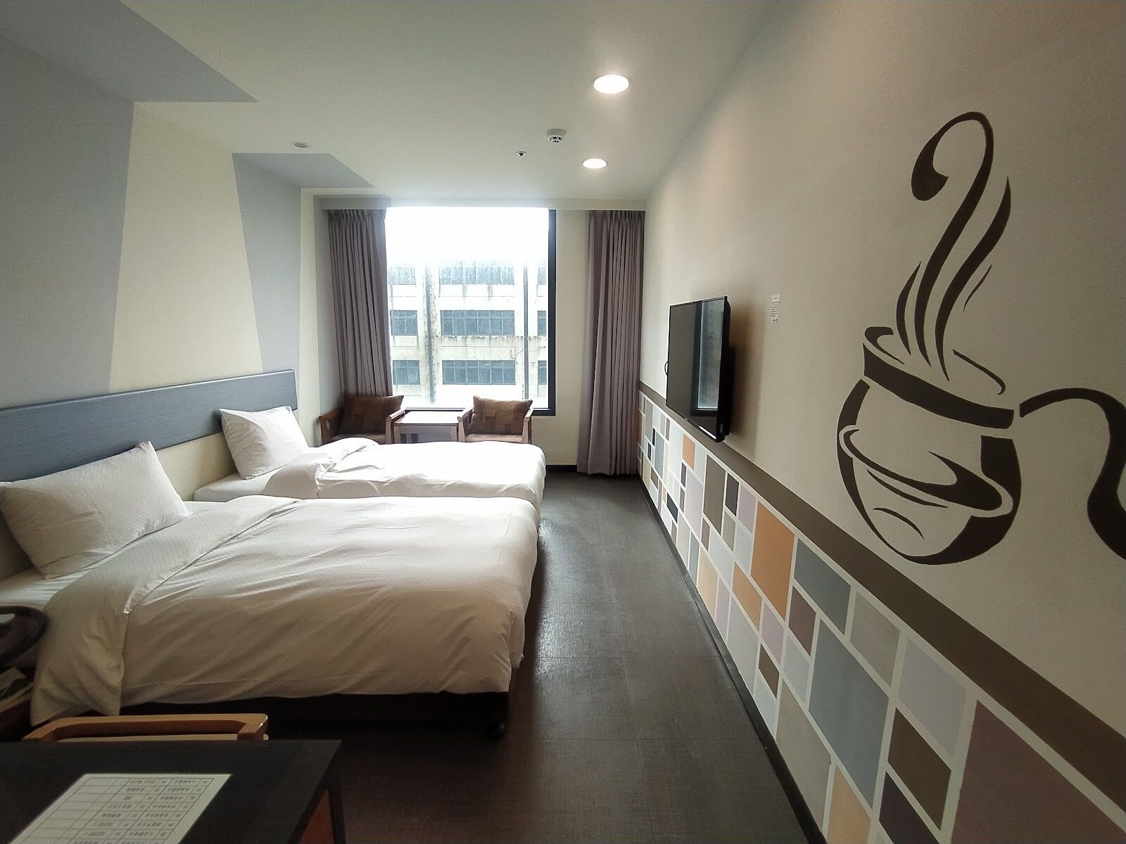 A hotel room with two beds, a TV, a small table, and a window with curtains.