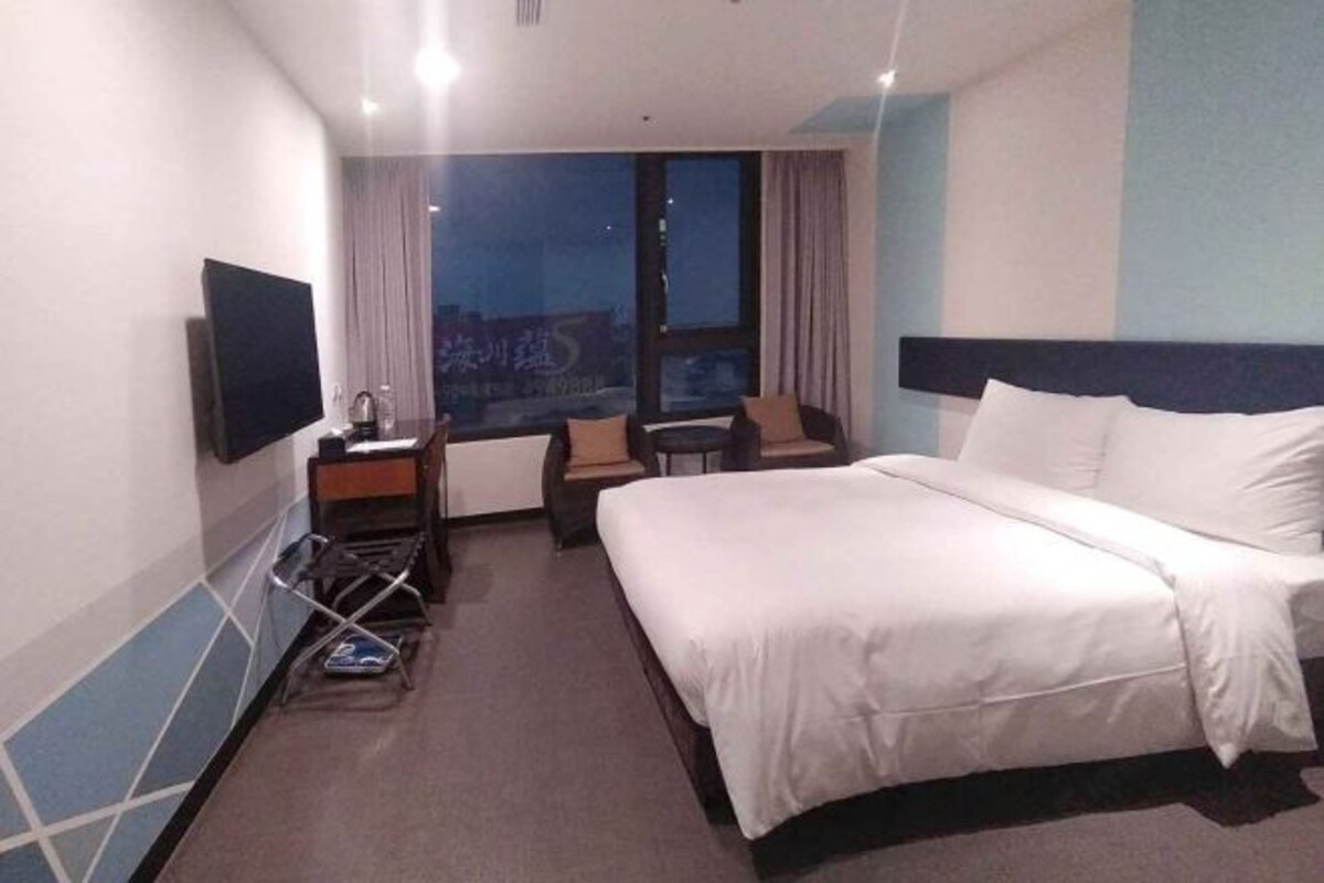 A hotel room with a bed, a desk, a chair, a TV, and a window with a view.