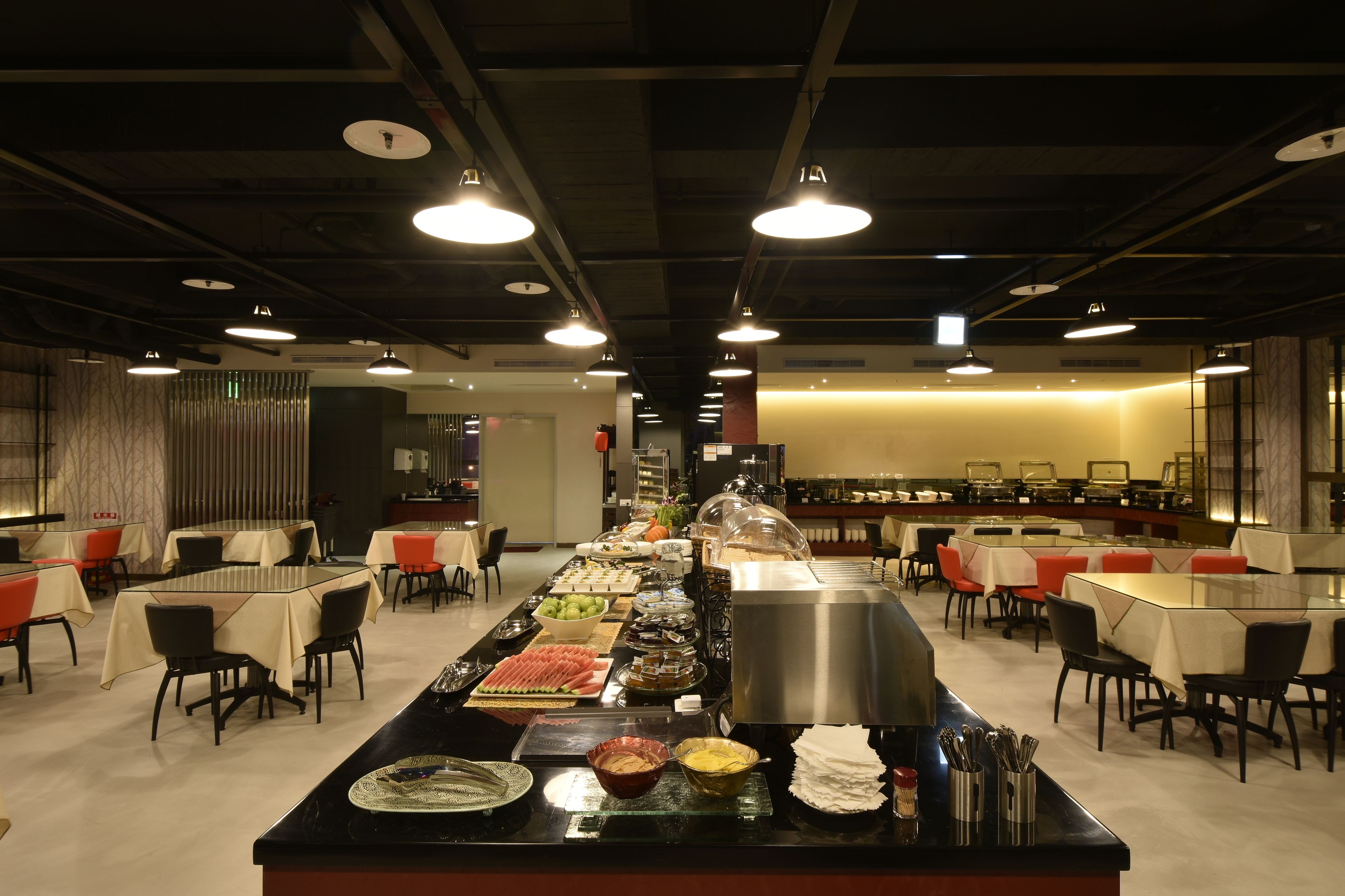 Ein reichhaltiges Buffet mit verschiedenen Speisen und einer Servierstation in einem geräumigen Speisesaal mit Tischen und Stühlen.
