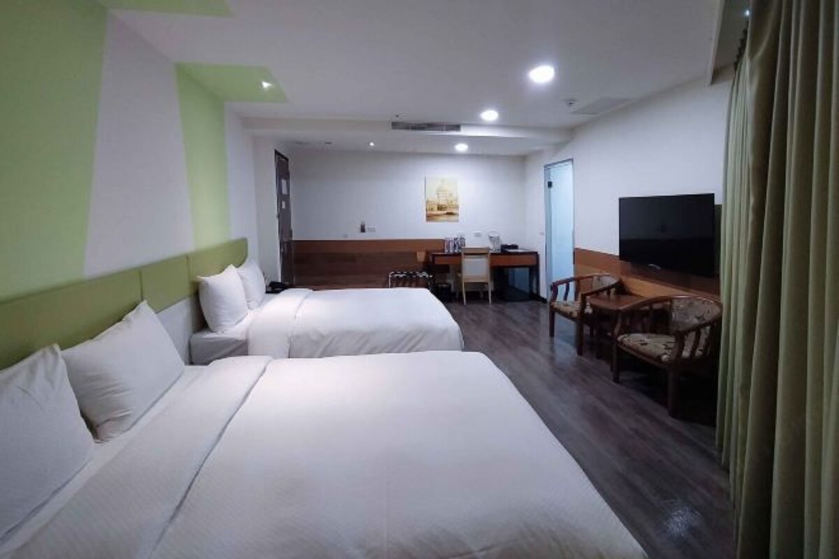 A hotel room with two beds, a desk, a chair, a television, and a door.