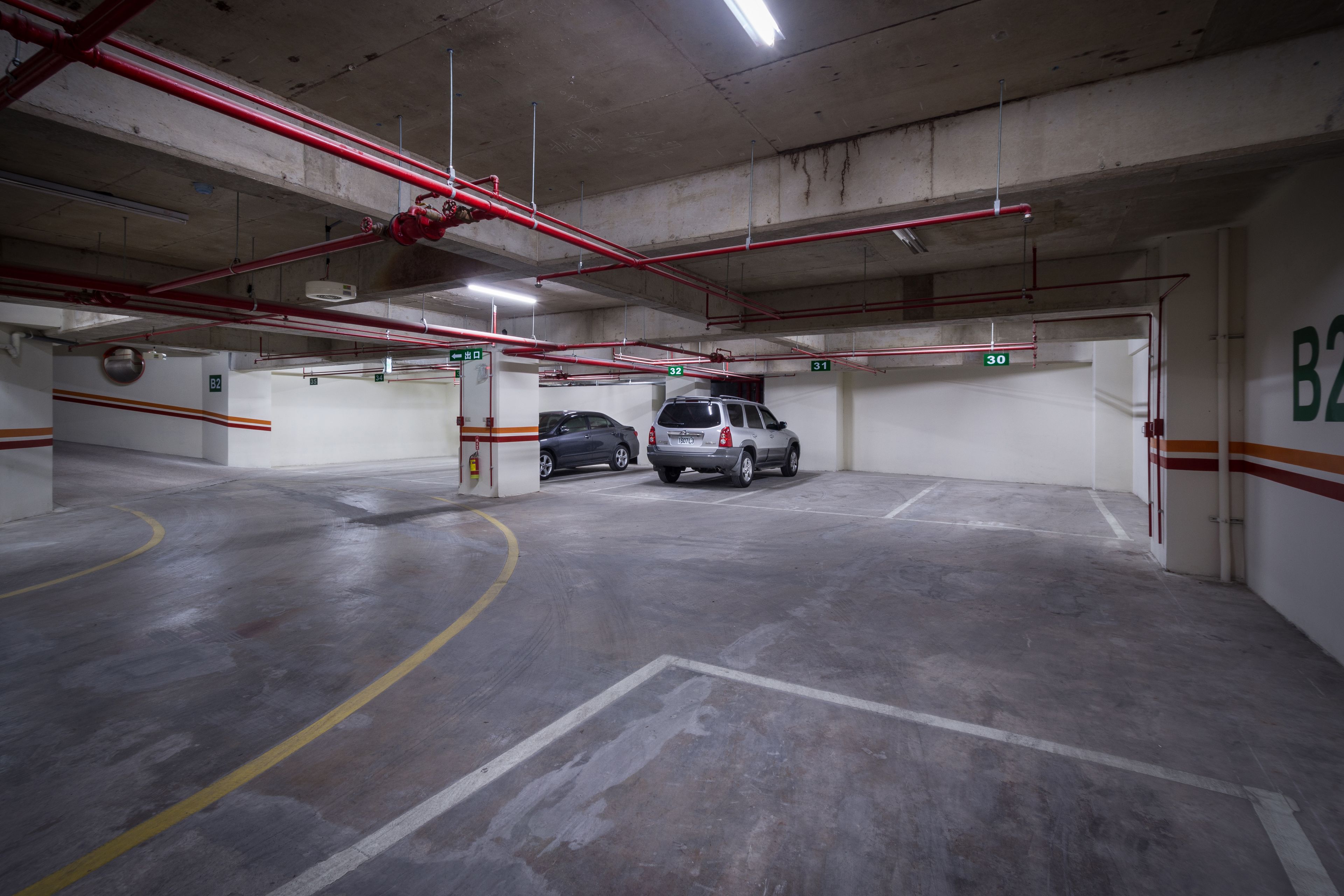 En parkeringskælder med betongulve, røde rør og nummererede parkeringspladser.