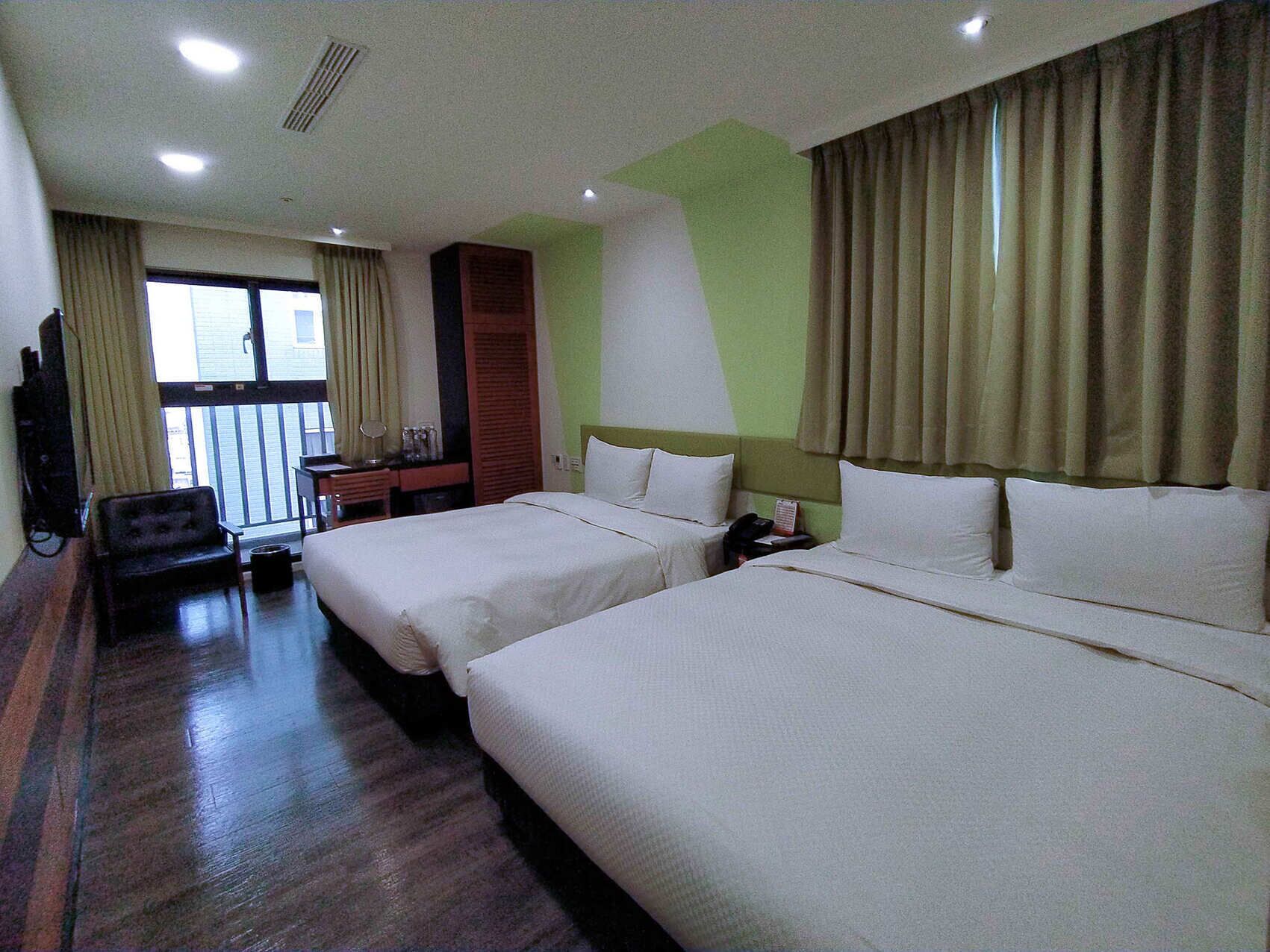 Habitació d'hotel amb dos llits, un escriptori, una cadira i una finestra amb cortines.