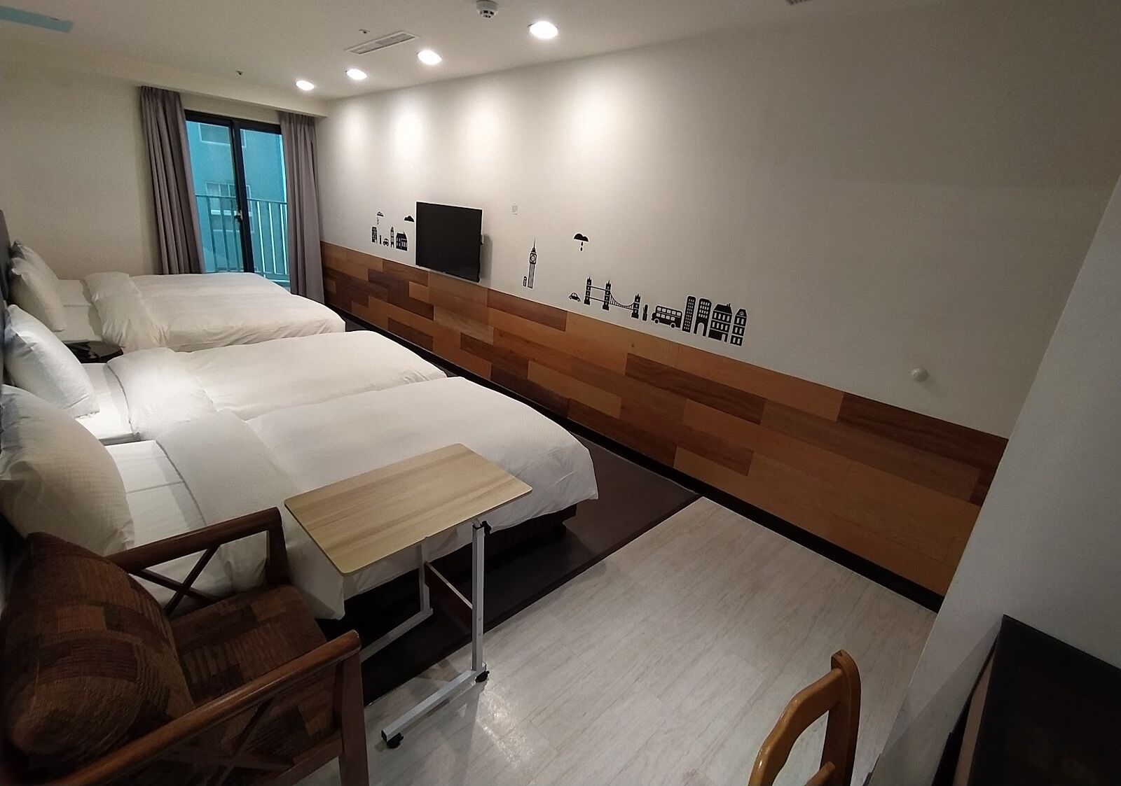 A hotel room with a large bed, a small table, and a cityscape mural on the wall.