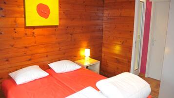 A room with wooden walls, a bed with orange bedding, white pillows, and a bedside table with a lamp.