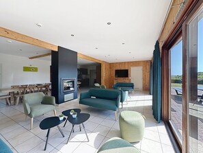 A spacious living area with a modern fireplace, comfortable seating, and a large window offering a view. - Holiday Home in Houyet with Private Sauna (Hour)