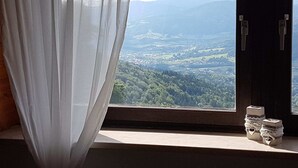 Ein Zimmer mit Fensterblick auf ein Tal, einem Vorhang und einem kleinen Tisch mit Dekoration.