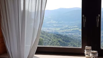 A room with a window overlooking a valley, a curtain, and a small table with decorative items.