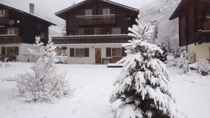 A chalet-style building with a balcony, surrounded by snow-covered trees and a snowy landscape.