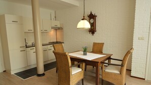 A dining area with a wooden table and wicker chairs, a hanging light fixture, and a kitchen in the background. - Modern Apartment in Schin op Geul near Valkenburg (Schin op Geul)