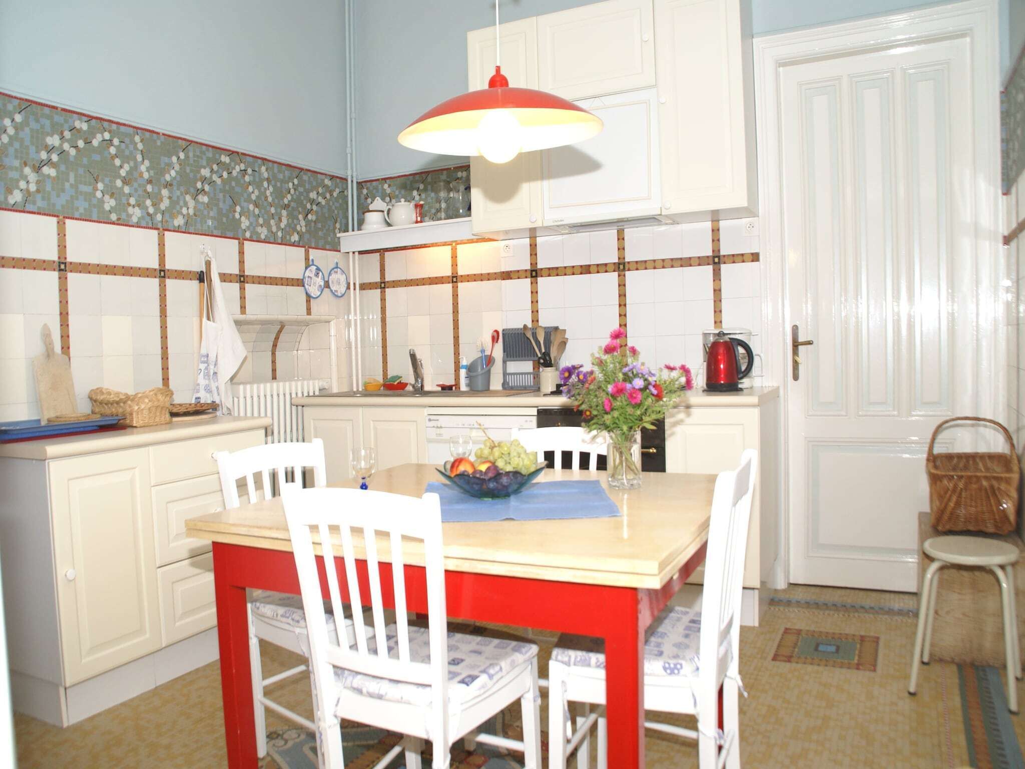 A kitchen with white cabinets, a red table, and a hanging light.