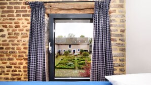 A room with a bed, a window with checkered curtains, and a view of a brick building and garden. - Pleasing Holiday Home in Richelle with Garden, Terrace, BBQ (Richelle)