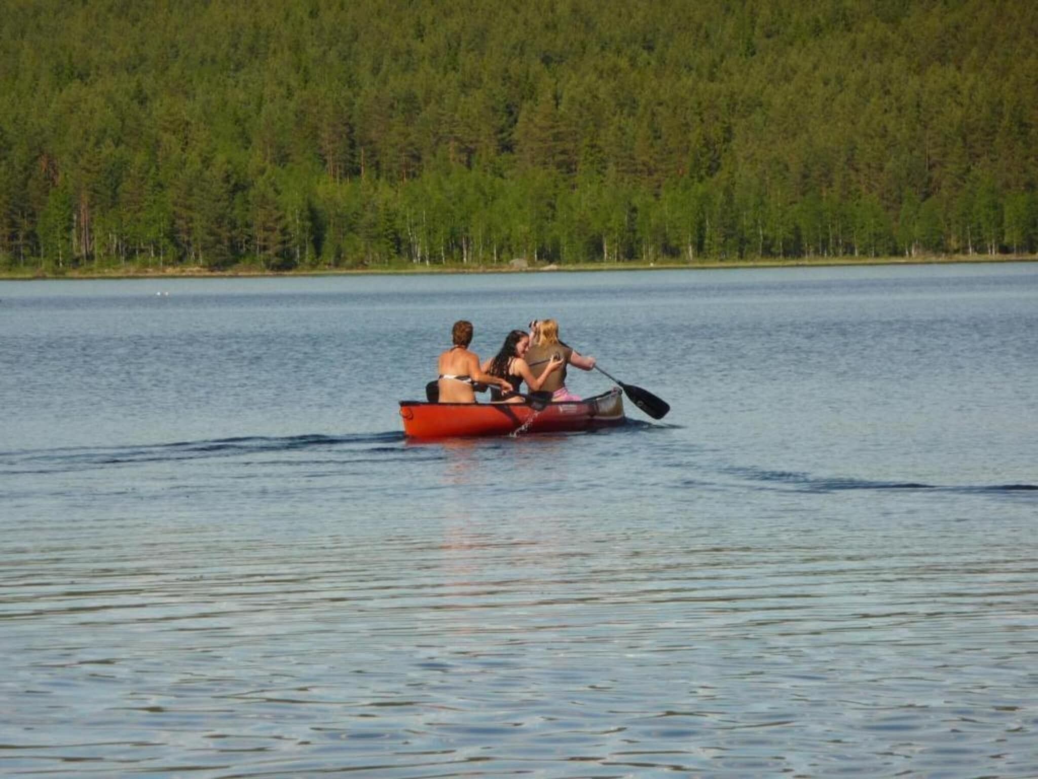 Un couple se trouve dans un petit bateau rouge sur un lac paisible, dont les rives sont bordées d’une forêt.