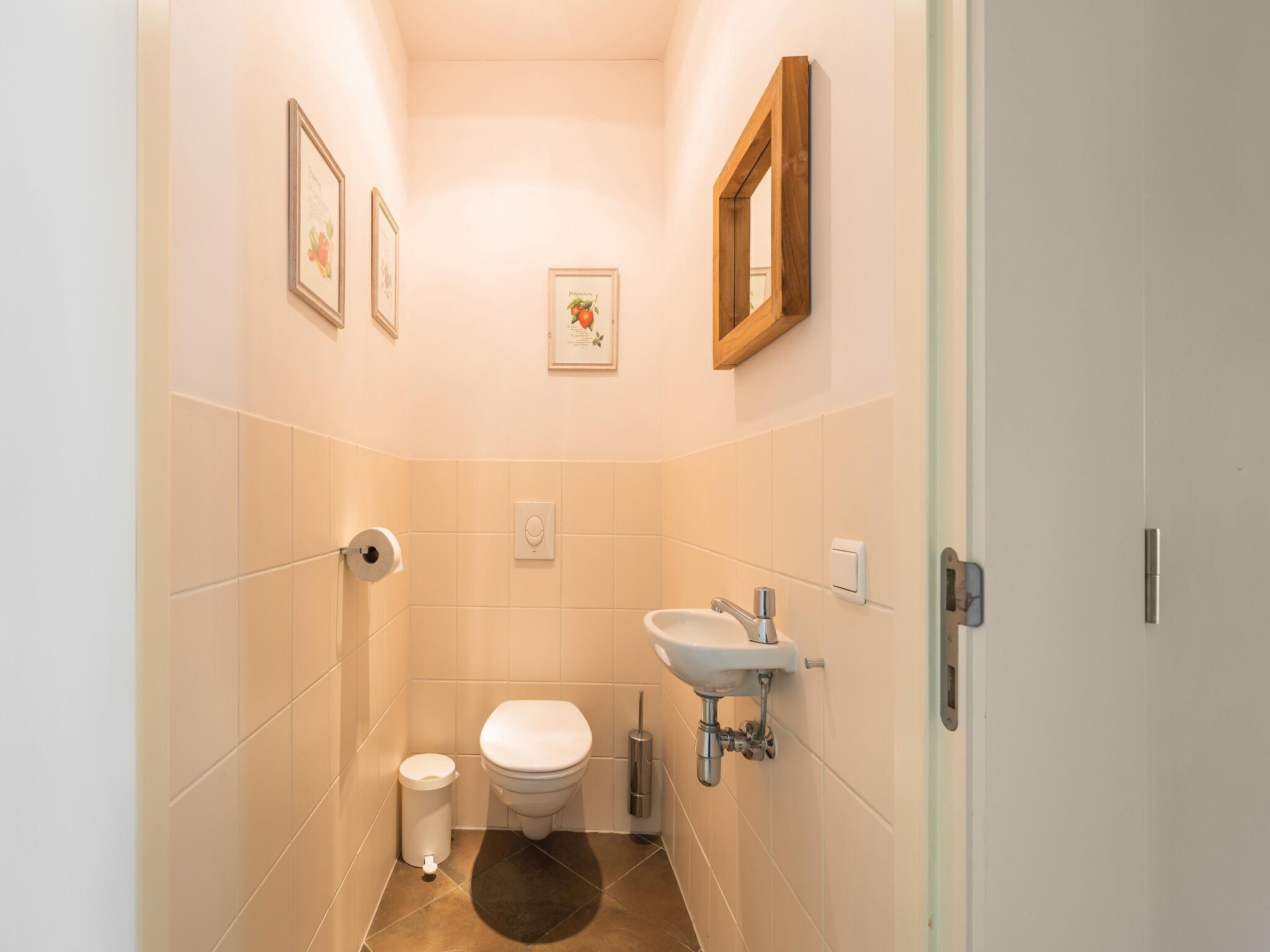 A small, narrow bathroom with a toilet, sink, and two framed pictures on the walls.