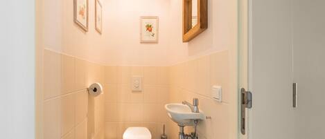 A small, narrow bathroom with a toilet, sink, and two framed pictures on the walls.