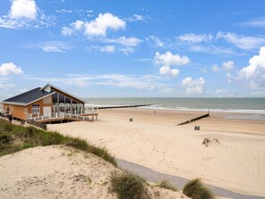 A beach house with a deck overlooking the ocean, a sandy beach, and a wooden pier.