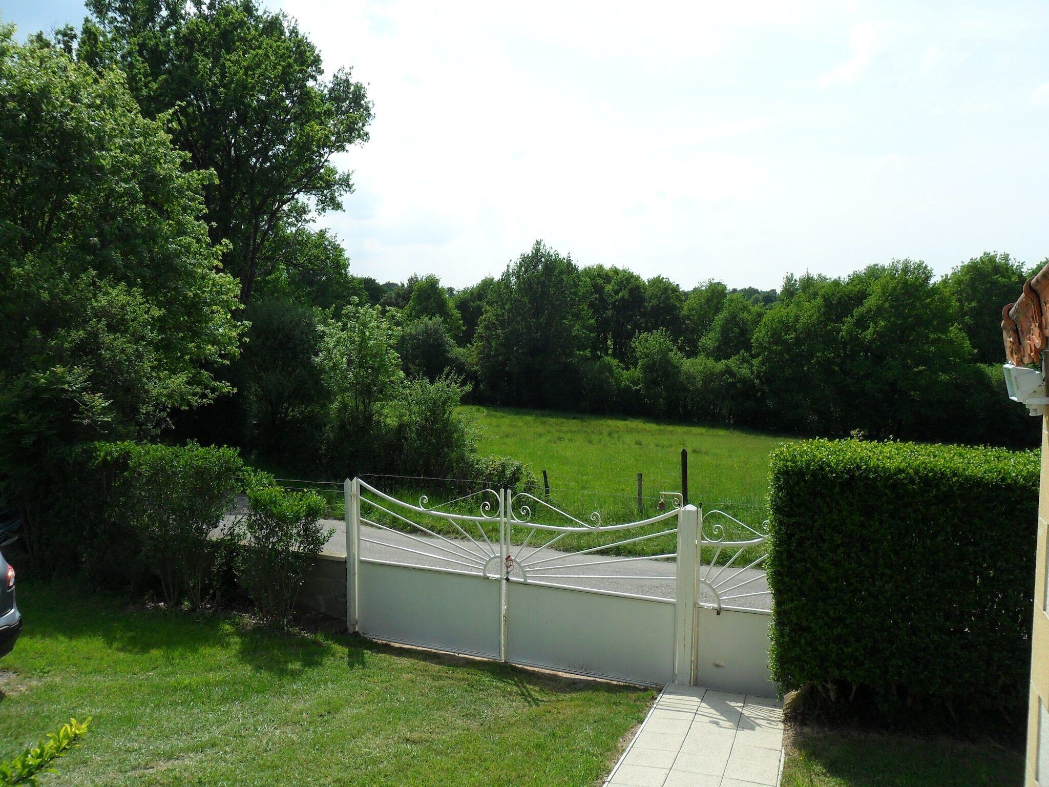 A gated property with a paved pathway leading to a green lawn and dense trees in the background.