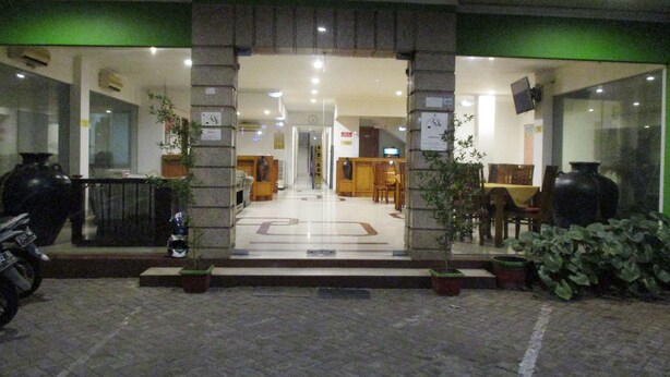 Entrada de hotel con recepción, área de descanso y plantas en macetas.