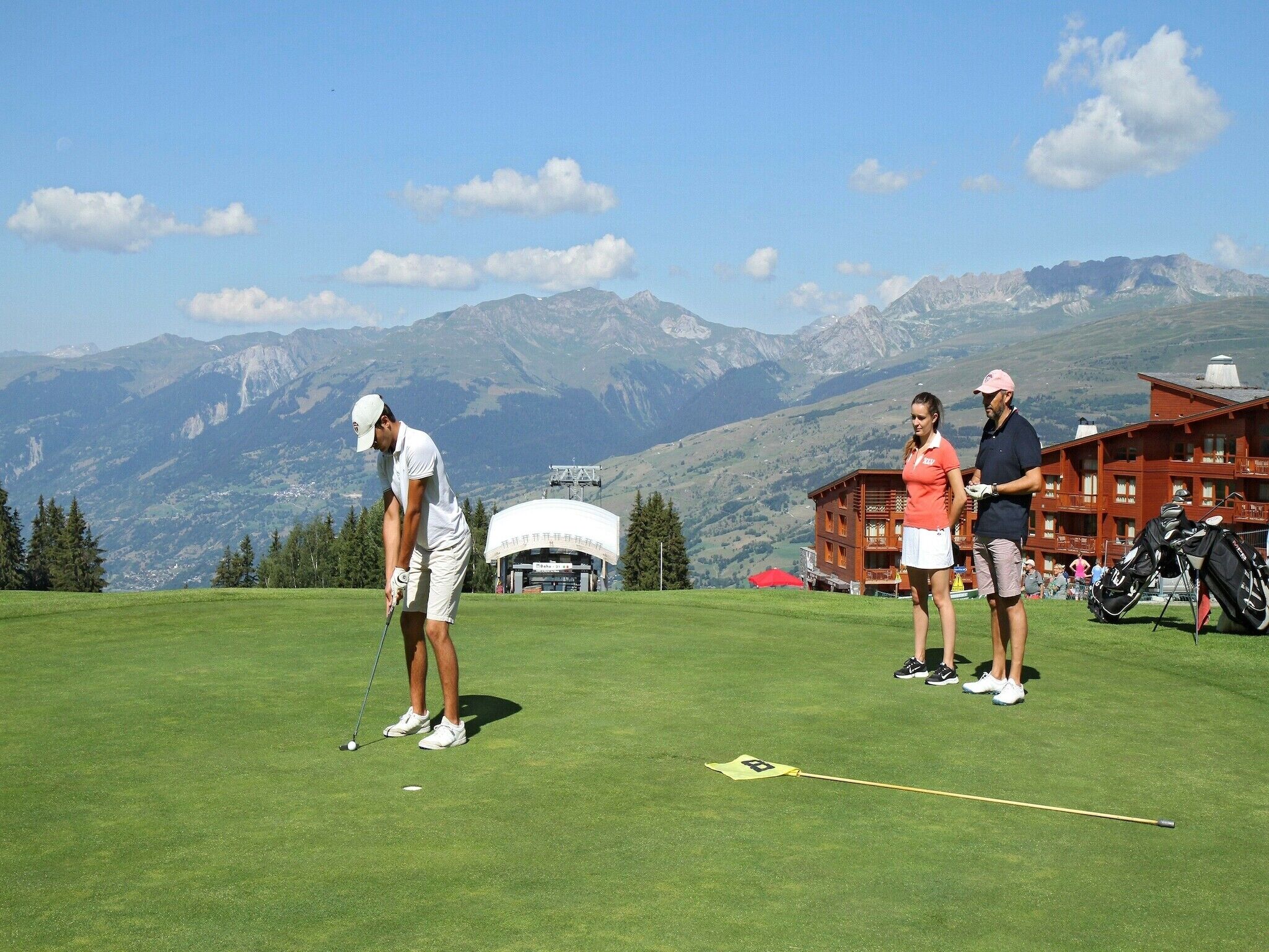A golf course with a mountainous backdrop, a lodge with a red facade, and a clear sky.