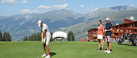 Un parcours de golf avec une chaîne de montagnes en arrière-plan, un chalet à la façade rouge et un ciel dégagé.