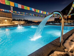 A pool with a waterfall feature, surrounded by stone walls and a night sky.