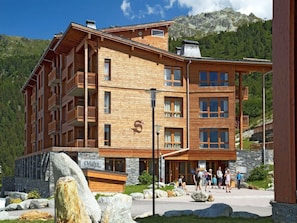Ein mehrstöckiges Holzgebäude mit Balkonen, einem Steinsockel und einer Bergkulisse.